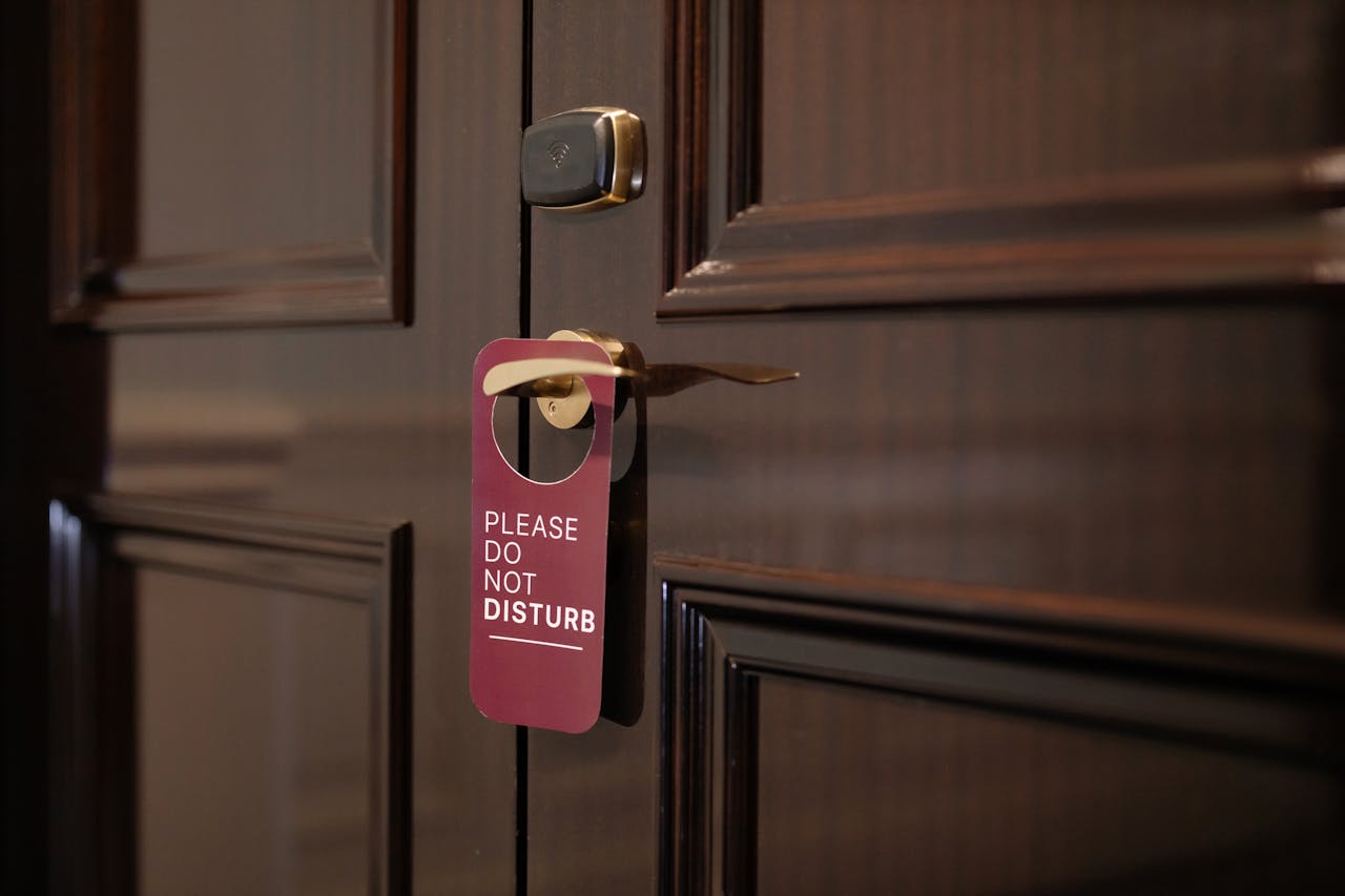 A wooden hotel door with a 'Please Do Not Disturb' sign hanging on the handle.